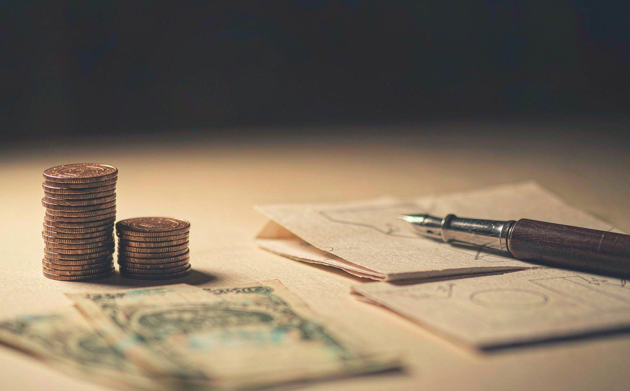 Two stacks of coins of different heights beside printed financial charts on a desk