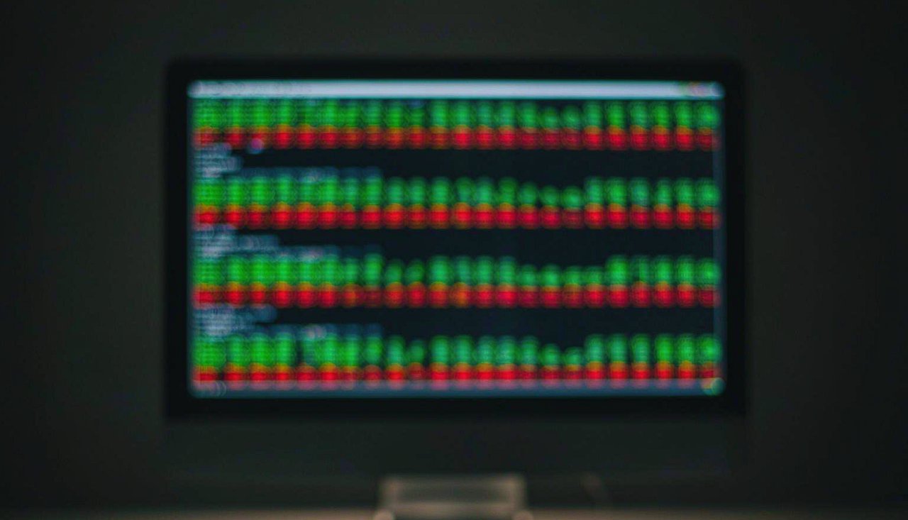 Stock charts and green and red figures glowing on a trading terminal screen in a dimly lit room