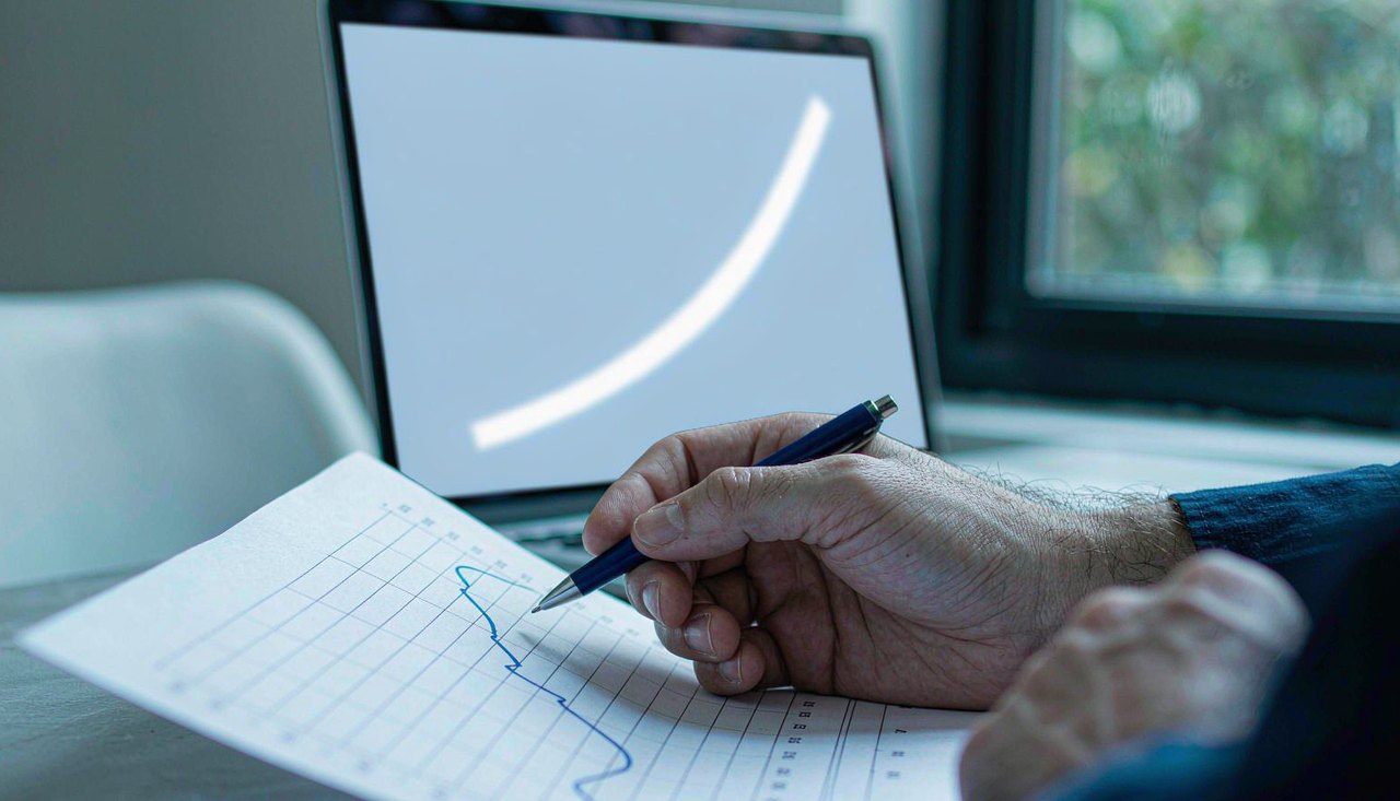 A printed interest rate chart and a coffee cup on a desk beside a computer screen showing a yield curve in daylight
